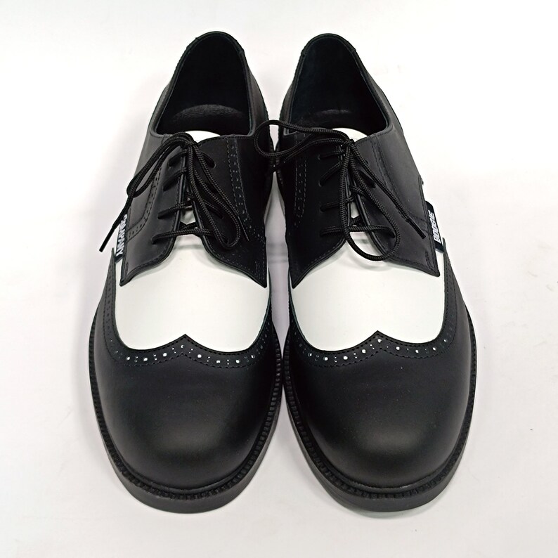 May include: A pair of black and white leather shoes with a wingtip design and a lace-up closure.