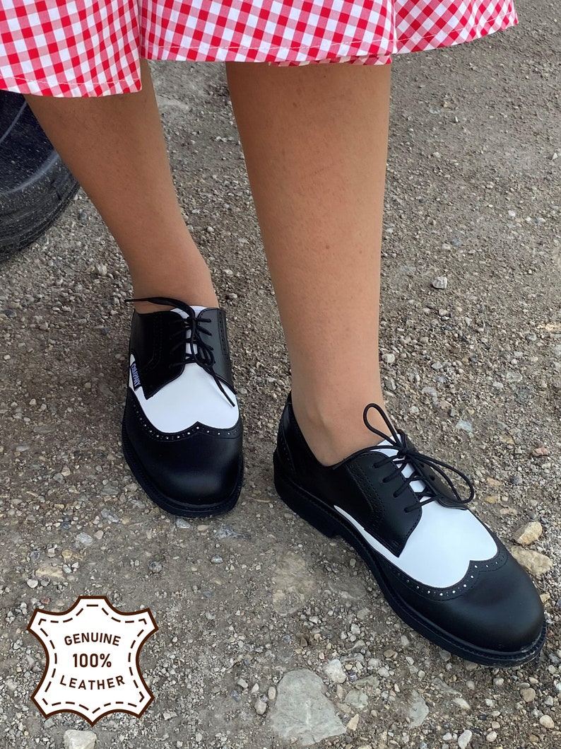 May include: Black and white leather oxford shoes with a wingtip design and black laces. The shoes are made of genuine leather and have a thick sole.