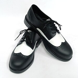 May include: A pair of black leather shoes with white wingtip detailing. The shoes have a lace-up closure and a brogue design.