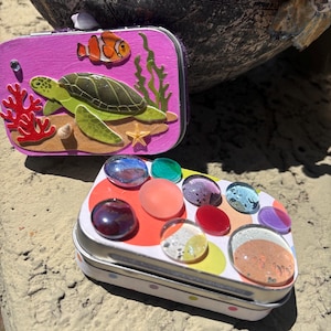 Cajas de tesoro coloridas y llamativas. Lata de metal morado y rosa con tortuga marina y burbujas de vidrio multicolor. Recipientes de regalo playeros hechos a mano.
