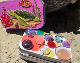 Cajas de tesoro coloridas y llamativas. Lata de metal morado y rosa con tortuga marina y burbujas de vidrio multicolor. Recipientes de regalo playeros hechos a mano.