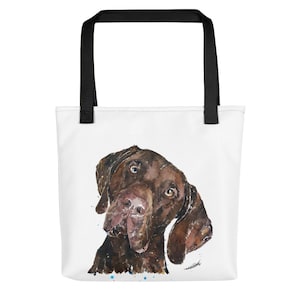 Puede incluir: Una bolsa de tela blanca con asas negras presenta una pintura de acuarela de un perro marrón mirando hacia arriba con una expresión curiosa. El pelaje del perro está pintado con una pincelada texturizada, y el fondo está acentuado con puntos de colores.