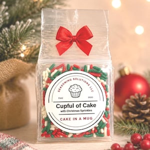 May include: A clear plastic bag filled with red, white, and green sprinkles, topped with a red ribbon bow. A circular white label features the text Seasoning Solutions LLC, Estd 2020, Cupful of Cake with Christmas Sprinkles, and CAKE IN A MUG.