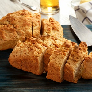 May include: A close-up of a blue wooden chopping board with two loaves of freshly baked bread sliced into pieces. The bread is golden brown and has a slightly crispy crust.