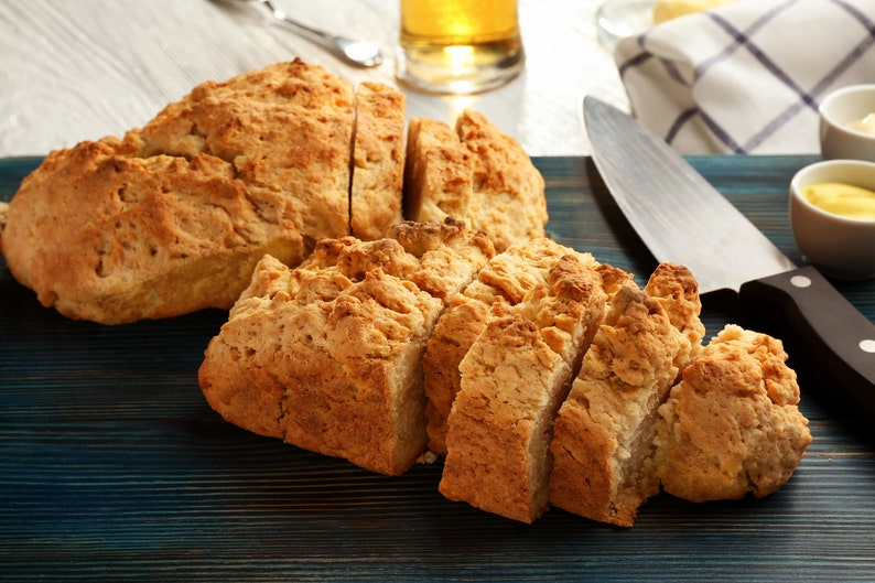 May include: A close-up of a blue wooden chopping board with two loaves of freshly baked bread sliced into pieces. The bread is golden brown and has a slightly crispy crust.