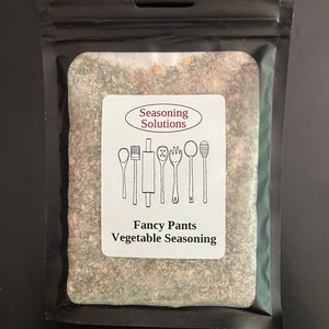 May include: A black resealable pouch with a white label that says "Seasoning Solutions" and "Fancy Pants Vegetable Seasoning". The label has a drawing of kitchen utensils. The pouch contains a brown and green seasoning blend.
