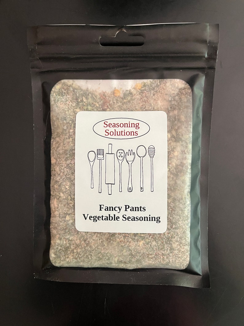 May include: A black resealable pouch with a white label that says "Seasoning Solutions" and "Fancy Pants Vegetable Seasoning". The label has a drawing of kitchen utensils. The pouch contains a brown and green seasoning blend.