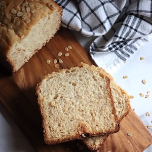 May include: A loaf of oat bread sliced on a wooden cutting board. The bread is light brown and has a soft texture. The cutting board is made of wood and has a natural finish.