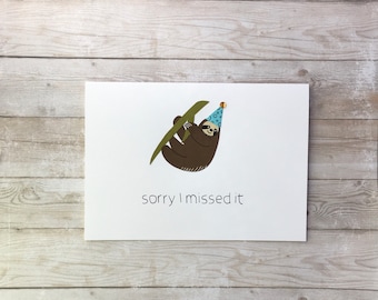 May include: A white card with a brown sloth wearing a blue party hat hanging from a green branch. The text "sorry I missed it" is printed below the sloth.