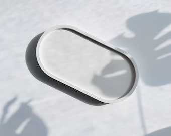 May include: White oval-shaped tray with a smooth, slightly raised rim. The tray is made of a solid material and has a matte finish.