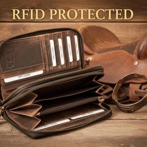 May include: A brown leather zip-around wallet with multiple interior card slots and compartments. The wallet features an embossed RFID PROTECTED logo on the interior panel. The wallet is open, revealing a dark brown fabric lining and several white credit card inserts.