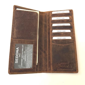 May include: A brown leather long wallet featuring multiple vertical credit card slots, a clear ID window, and a large currency compartment. The interior is embossed with the text Sedona USA, RFID, and Buffalo Leather, with a card insert present.
