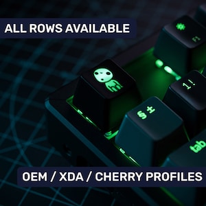 May include: A black mechanical keyboard with green backlighting. The keyboard has a keycap with a white graphic of a cartoon character. The text "ALL ROWS AVAILABLE" and "OEM / XDA / CHERRY PROFILES" is visible on the keyboard.