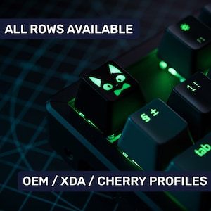 Può includere: Una tastiera meccanica nera con retroilluminazione verde. La tastiera ha un cappuccio per tasti a forma di gatto con un papillon. Il testo "ALL ROWS AVAILABLE" e "OEM/XDA/CHERRY PROFILES" è visibile nell'immagine.