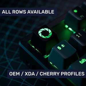 Può includere: Una tastiera meccanica nera con retroilluminazione verde. La tastiera ha un cappuccio del tasto con un'icona dell'otturatore della fotocamera verde. Il testo "ALL ROWS AVAILABLE" e "OEM / XDA / CHERRY PROFILES" è visibile nell'immagine.