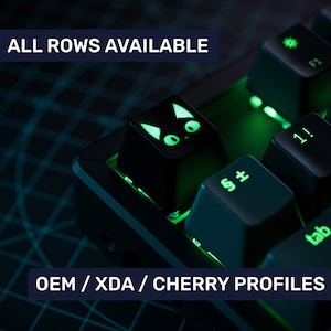 Op de afbeelding: Een zwart mechanisch toetsenbord met groene achtergrondverlichting. Het toetsenbord heeft een kattenvormige toetsdop met groene ogen. De tekst "ALL ROWS AVAILABLE" en "OEM / XDA / CHERRY PROFILES" is zichtbaar op de afbeelding.