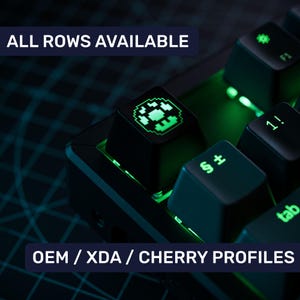 May include: A close-up of a black mechanical keyboard with green backlighting. The keyboard has a keycap with a green pixelated design. The text "ALL ROWS AVAILABLE" and "OEM/XDA/CHERRY PROFILES" is visible in the image.