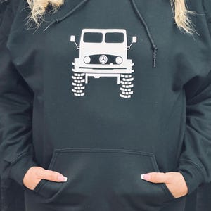 May include: Black hooded sweatshirt with a white graphic of a vintage off-road vehicle.