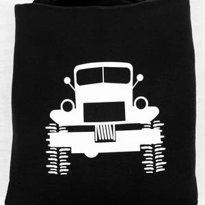 May include: Black hoodie with a white silhouette of a truck with large tires. The truck has a simple design with a rectangular body and a rounded front.