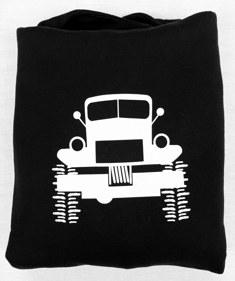 May include: Black hoodie with a white silhouette of a truck with large tires. The truck has a simple design with a rectangular body and a rounded front.