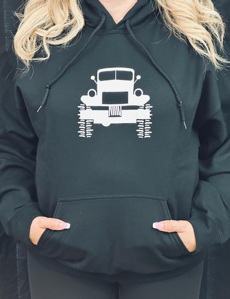 May include: Black hooded sweatshirt with a white graphic of a vintage truck. The truck has a large grill and headlights. The sweatshirt has a kangaroo pocket.