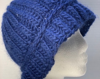 May include: A navy blue knitted hat with a brim. The hat is made of thick yarn and has a textured, ribbed design. The hat is displayed on a white mannequin head.