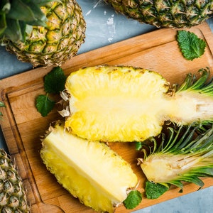 May include: A close-up of a pineapple cut in half, revealing the yellow flesh. The pineapple is on a wooden cutting board with green leaves.
