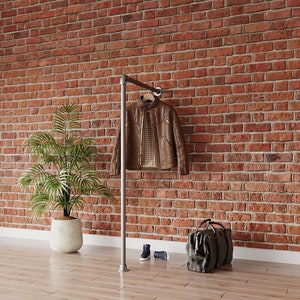 May include: A brown leather jacket hangs on a metal clothing rack against a red brick wall. A brown leather duffel bag sits on the floor next to a pair of blue trainers.