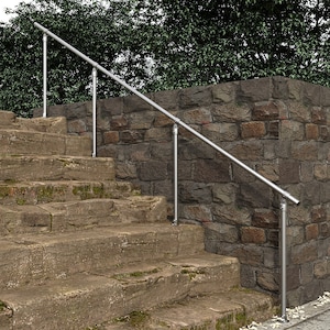 Op de afbeelding: Een zilveren handrail is gemonteerd aan een stenen muur en stenen trappen. De handrail is gemaakt van metalen buizen en is met beugels aan de muur bevestigd.