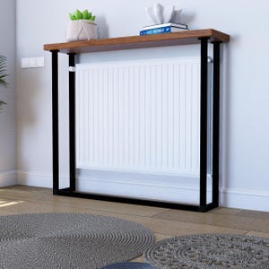 Può includere: Una consolle moderna con piano in legno scuro e struttura in metallo nero. Un radiatore bianco è integrato. Il tavolo è contro un muro bianco, con oggetti decorativi e tappeti rotondi sul pavimento.