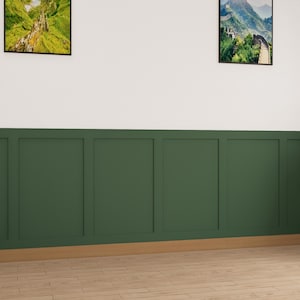 May include: A wall with a white top half and a dark green bottom half. The bottom half is divided into six panels with a wood trim around the edges. There are two framed pictures on the wall, one above the other. The top picture is a landscape scene with green hills and a waterfall. The bottom picture is a landscape scene with a mountain range. There is a potted plant in the corner of the room.