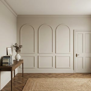 Könnte beinhalten: Ein Innenraum mit beigen Wänden, drei bogenförmigen Wandverkleidungen, einem Holzkonsolentisch mit Büchern und einer weißen Vase mit Trockenblumen, einer geschlossenen Tür mit Messinggriff sowie einem Fischgrätparkett mit einem Juteteppich.