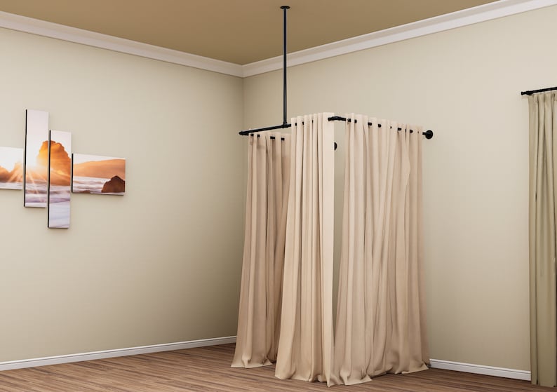 Puede incluir: Un sistema de barra de cortina de metal negro con cortinas beige colgadas. La barra est&aacute; unida al techo y se extiende para crear un recinto cuadrado.