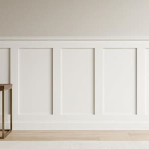 May include: A decorative vase with a speckled, light brown finish sits on a dark wood table with a gold metal frame. The table is placed in front of a white paneled wall. The room has a neutral color palette and a minimalist aesthetic.