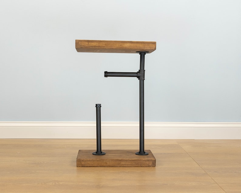 May include: A rustic side table with a wooden top and base, connected by black metal pipes. The table has a unique industrial design, perfect for a living room or bedroom. The wooden top measures approximately 12 inches long.