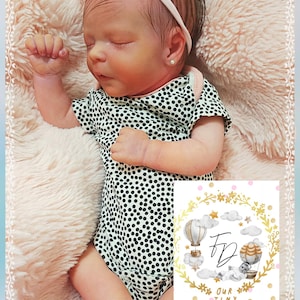 May include: A sleeping baby wearing a black and white polka dot onesie and a pink headband. The baby is lying on a fluffy, pink blanket. A card with the text "OUR TINY HUMAN" and a hot air balloon illustration is in the image.