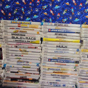 K&ouml;nnte beinhalten: Ein Stapel von &uuml;ber 30 Videospiel-H&uuml;llen f&uuml;r die Nintendo Wii-Konsole. Die H&uuml;llen sind gr&ouml;&szlig;tenteils wei&szlig; mit bunten Spieltiteln und Logos. Einige der Spiele sind "Just Dance 2014", "Star Wars III", "Spider-Man Shattered Dimensions", "Build'n Race", "FIFA Soccer 09", "NBA Live 08", "Sonic Unleashed", "My Sims Kingdom", "Super Mario Galaxy", "The Legend of Zelda Twilight Princess", "Star Wars III The Clone Wars", "Boom Blox Bash Party", "Dance on Broadway", "FIFA Soccer 11" und "Wii Sports".