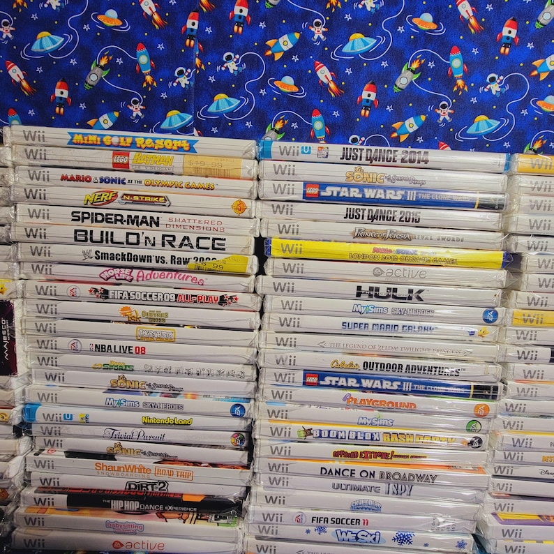 K&ouml;nnte beinhalten: Ein Stapel von &uuml;ber 30 Videospiel-H&uuml;llen f&uuml;r die Nintendo Wii-Konsole. Die H&uuml;llen sind gr&ouml;&szlig;tenteils wei&szlig; mit bunten Spieltiteln und Logos. Einige der Spiele sind "Just Dance 2014", "Star Wars III", "Spider-Man Shattered Dimensions", "Build'n Race", "FIFA Soccer 09", "NBA Live 08", "Sonic Unleashed", "My Sims Kingdom", "Super Mario Galaxy", "The Legend of Zelda Twilight Princess", "Star Wars III The Clone Wars", "Boom Blox Bash Party", "Dance on Broadway", "FIFA Soccer 11" und "Wii Sports".