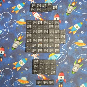 May include: An assortment of black Sony PS Vita memory cards, with varying storage capacities, arranged on a blue fabric patterned with rockets, planets, and stars. The cards are labeled with the Sony and PS Vita logos and storage sizes.
