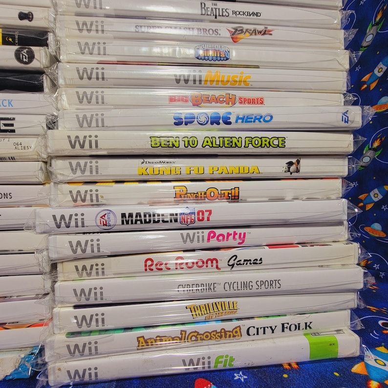 K&ouml;nnte beinhalten: Ein Stapel von 15 Videospiel-H&uuml;llen f&uuml;r die Nintendo Wii-Konsole. Die H&uuml;llen sind wei&szlig; mit bunten Spieltiteln und Logos. Die Titel umfassen "Wii Music", "Big Beach Sports", "Spore Hero", "Ben 10 Alien Force", "Kung Fu Panda", "Punch-Out!!", "Madden NFL 07", "Wii Party", "Rec Room Games", "Cyberbike Cycling Sports", "Thrillville Off the Rails", "Animal Crossing City Folk" und "Wii Fit".