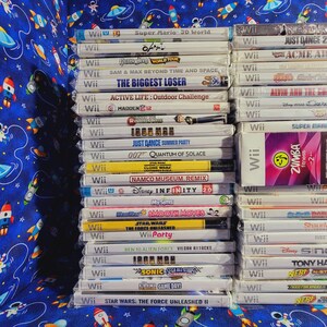 K&ouml;nnte beinhalten: Ein Stapel von Videospiel-Kartuschen f&uuml;r die Nintendo Wii-Konsole. Die Kartuschen sind vertikal angeordnet und beinhalten Titel wie "Super Mario 3D World", "Just Dance 2", "O'Mally", "Acme Arcade", "The Biggest Loser", "Active Life: Outdoor Challenge", "Madden 12", "Iron Man", "Just Dance Summer Party", "007 Quantum of Solace", "Namco Museum Remix", "Disney Infinity 2.0", "MySims", "Smooth Moves", "Star Wars: The Force Unleashed", "Wii Party", "Ben 10 Alien Force: Vilgax Attacks", "Iron Man", "Sonic Sega All-Stars", "Club Game Day", "Star Wars: The Force Unleashed II", "Zumba Fitness 2", "Shaun White Snowboarding", "Disney Sing It", "Tony Hawk: Ride", "Nerf N-Strike", "Need for Speed: Hot Pursuit" und "Nerf N-Strike".