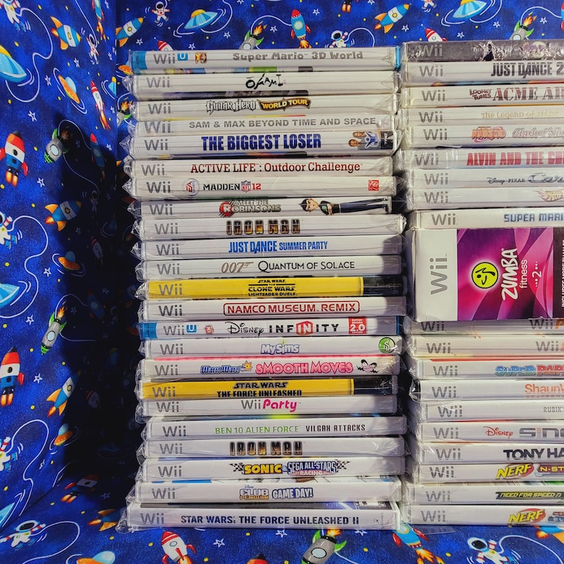 K&ouml;nnte beinhalten: Ein Stapel von Videospiel-Kartuschen f&uuml;r die Nintendo Wii-Konsole. Die Kartuschen sind vertikal angeordnet und beinhalten Titel wie "Super Mario 3D World", "Just Dance 2", "O'Mally", "Acme Arcade", "The Biggest Loser", "Active Life: Outdoor Challenge", "Madden 12", "Iron Man", "Just Dance Summer Party", "007 Quantum of Solace", "Namco Museum Remix", "Disney Infinity 2.0", "MySims", "Smooth Moves", "Star Wars: The Force Unleashed", "Wii Party", "Ben 10 Alien Force: Vilgax Attacks", "Iron Man", "Sonic Sega All-Stars", "Club Game Day", "Star Wars: The Force Unleashed II", "Zumba Fitness 2", "Shaun White Snowboarding", "Disney Sing It", "Tony Hawk: Ride", "Nerf N-Strike", "Need for Speed: Hot Pursuit" und "Nerf N-Strike".