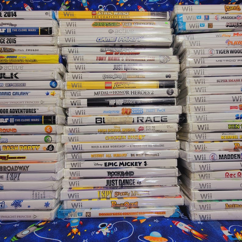 K&ouml;nnte beinhalten: Ein Stapel von &uuml;ber 20 Videospiel-H&uuml;llen f&uuml;r die Nintendo Wii-Konsole. Die H&uuml;llen sind gr&ouml;&szlig;tenteils wei&szlig; mit bunten Spieltiteln und Logos. Einige der Spiele sind Star Wars, Jurassic Park, Spider-Man, Tony Hawk's, Just Dance, Lego Indiana Jones, Medal of Honor, Hip Hop Dance, High School Musical, Chicken Dance, Build-A-Bear Workshop, Destroy All Humans, Epic Mickey, Rock Band, Just Dance 4, iSpy, Donkey Kong Country Returns, Madden, Minecraft und mehr.