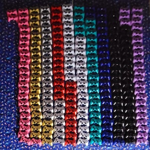 May include: A collection of 14 rows of miniature video game controllers in various colors, including pink, gold, silver, red, teal, blue, black, and purple.