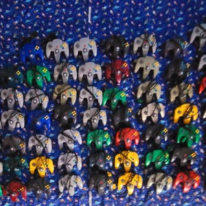 May include: A collection of colorful Nintendo 64 controllers, arranged in rows on a blue patterned surface. The controllers are in various colors, including green, blue, red, and gray.