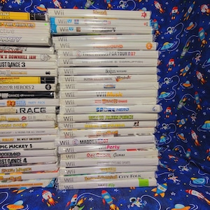 K&ouml;nnte beinhalten: Ein Stapel von 20 Videospiel-H&uuml;llen f&uuml;r die Nintendo Wii-Konsole. Die H&uuml;llen sind wei&szlig; mit bunten Spieltiteln und Logos. Die Spiele beinhalten Titel wie "Madden 07", "Just Dance 3", "Spore Hero" und "Rec Room Games".