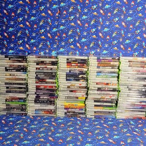 Può includere: Una grande collezione di videogiochi, tutti nelle loro custodie, impilati su uno scaffale. I giochi sono tutti per la console Xbox 360. Le custodie sono principalmente verdi e nere, con alcuni accenti rossi e blu.