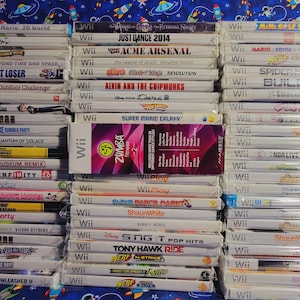 K&ouml;nnte beinhalten: Ein Stapel von &uuml;ber 30 Videospiel-H&uuml;llen f&uuml;r die Nintendo Wii-Konsole. Die H&uuml;llen sind gr&ouml;&szlig;tenteils wei&szlig; mit bunten Spieltiteln und Logos. Einige der Spiele sind Just Dance 2014, Super Mario Galaxy, Zumba Fitness 2 und Tony Hawk Ride.