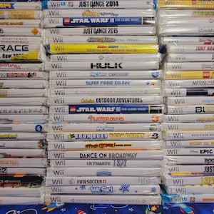 K&ouml;nnte beinhalten: Ein Stapel von 20 Videospiel-H&uuml;llen f&uuml;r die Nintendo Wii-Konsole. Die H&uuml;llen sind gr&ouml;&szlig;tenteils wei&szlig; mit bunten Spieltiteln und Logos. Einige der Spiele sind Just Dance 2014, Star Wars III: The Clone Wars, Super Mario Galaxy und The Legend of Zelda: Twilight Princess.