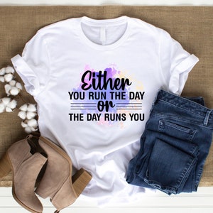 K&ouml;nnte beinhalten: Wei&szlig;es T-Shirt mit Aquarellhintergrund und dem Text "Either you run the day or the day runs you".